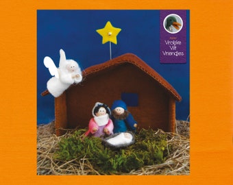 Op de afbeelding: Een vilten kerststal met een bruine stal, een gele ster en figuren die Maria, Jozef en het kindje Jezus voorstellen. Een engel vliegt boven de stal. De scène is geplaatst op groen mos en stro.