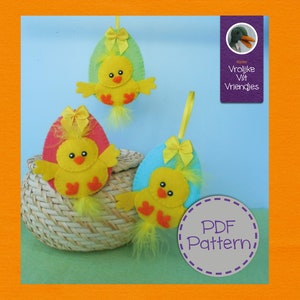 以下が含まれることがあります： 黄色いひよこが入ったフェルト製のイースターエッグのオーナメントが3つ。卵は緑、ピンク、青です。オーナメントは紐で吊り下げられており、籐のバスケットの前にあります。右下隅には紫色の円の中に「PDF Pattern」という文字が書かれています。右上隅には紫色の長方形の中に「Vrolijke Vilt Vriendjes」という文字が書かれています。