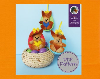Op de afbeelding: Drie vilten paaseieren-versieringen in de vorm van konijnen, met gele, rode en blauwe accenten. De versieringen zitten in een rieten mand met kleurrijke paaseieren. De tekst "PDF Pattern" staat op een paarse cirkel met een grijze stippellijn.