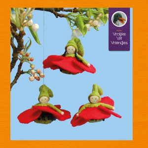 May include: Three felt dolls hanging from a tree branch. Each doll is wearing a green hat and a red felt skirt. The dolls are hanging from a string and are surrounded by white flowers.