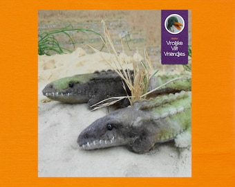 Op de afbeelding: Twee vilten alligator speelgoedjes, een groen en een bruin, liggend op een zanderig oppervlak met groen gras op de achtergrond. De tekst "Vrolijke Vilt Vriendjes" is zichtbaar in de rechterbovenhoek van de afbeelding.