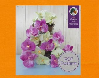 Op de afbeelding: Een PDF-patroon voor het maken van vilt orchideeën. Het patroon bevat instructies voor het maken van zowel roze als witte orchideeën. Het patroon is beschikbaar om te downloaden. De afbeelding bevat ook een klein beeld van een eend en de tekst "Atelier Vrolijke Vilt Vriendjes".