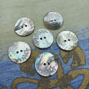 Peut inclure: Six boutons nacrés irisés avec un motif floral. Chaque bouton a deux trous et une surface subtile et chatoyante. Les boutons sont ronds et mesurent environ 2,5 cm de diamètre.