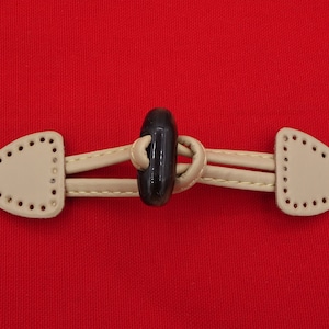 May include: A beige toggle closure with a black plastic button. The closure has two loops on either side of the button.
