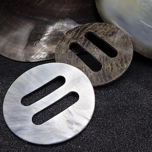 Könnte beinhalten: Drei runde, dekorative Metallschnallen mit einem Doppelschlitz-Design. Die Schnallen sind in den Farben Braun, Weiß und Silber.