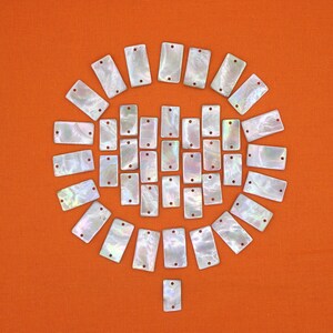 May include: A collection of white iridescent rectangular tiles arranged in a circular pattern on an orange background.