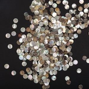 Peut inclure: Un grand groupe de pièces rondes en nacre irisée dans différentes nuances de brun et de blanc. Les pièces sont dispersées sur un fond noir.