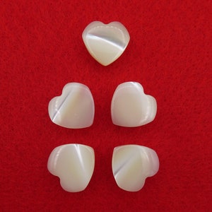 以下が含まれることがあります： 真珠光沢のある白いハート型のボタンが5つ。ボタンは赤いフェルトの背景にピラミッド型に配置されています。