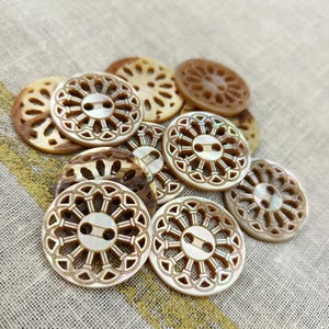 以下が含まれることがあります： 真珠貝で作られた丸い装飾ボタンのコレクション。ボタンは繊細で複雑なデザインで、薄い茶色をしています。