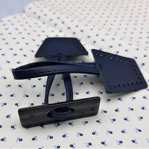 May include: A navy blue leather toggle clasp set, featuring a rectangular toggle and two square pieces with stitched holes for attachment. The clasp is designed for bags, coats, or other craft projects.