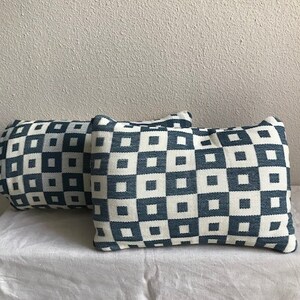 May include: Two decorative throw pillows with a geometric pattern of white and blue squares. The pillows are made of a soft, woven fabric.