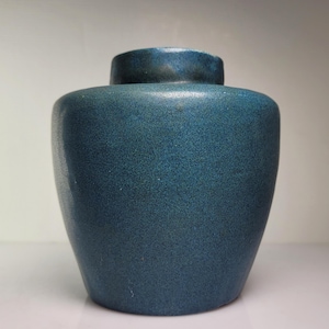 May include: A small, rounded ceramic jar with a deep blue, speckled glaze. The vessel features a wide, bulbous body that tapers slightly toward the base and a short, cylindrical neck with a flat rim, showcasing a consistent, textured finish.