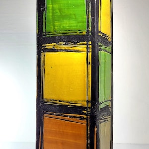May include: A rectangular, vertical decorative vase with a black frame and colorful panels. The panels are painted in shades of green, yellow, and orange. The vase is approximately 12 inches tall.