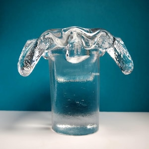 May include: A clear glass candle holder with a unique, wavy, ruffled top. The holder has a cylindrical base.