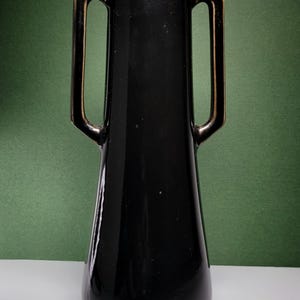 May include: A black ceramic vase with gold-trimmed handles. The vase has a narrow neck and a wide base.