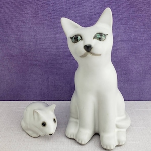 May include: White ceramic cat figurine with green eyes and a small white ceramic mouse figurine with black eyes.
