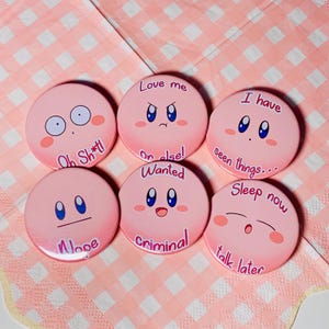 May include: Six pink round buttons with different cartoon faces and text. The text on the buttons reads: "Love me or else!", "I have seen things... Sleep now", "Ob Sh*t!", "Wanted criminal", "Nope", "Talk later".