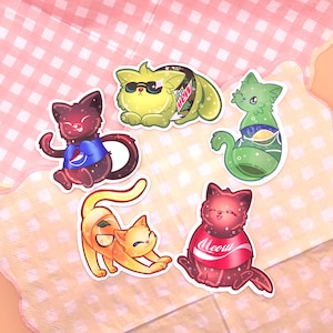 May include: Five colorful cat stickers with different soda and juice can designs. The cats are wearing the cans as clothing. The stickers are on a pink and white checkered background.