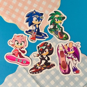 May include: A collection of six colorful stickers featuring characters from the Sonic the Hedgehog franchise. The stickers depict Sonic, Amy, Shadow, Jet, and Wave, each on a surfboard or skateboard. The background is blue and pink.