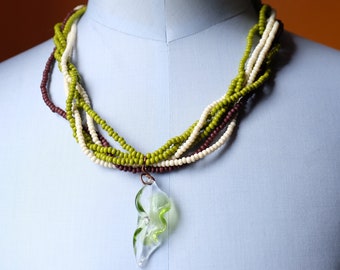 May include: A multi-strand necklace with green, white and brown beads. A green glass pendant shaped like a leaf hangs from the necklace.