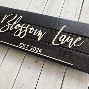 Puede incluir: Un letrero de madera negro con letras blancas que dice "Blossom Lane EST 2024".