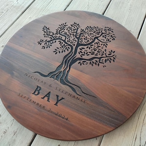May include: A round wooden serving tray with a tree design engraved into the surface. The text "Nicolas & Stephanie Bay September 2, 2024" is also engraved on the tray.