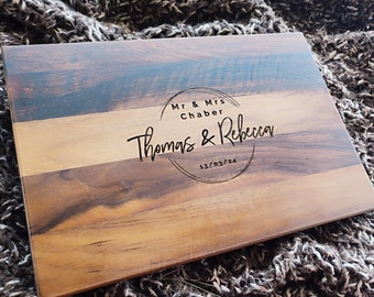 May include: A wooden cutting board with a natural wood grain finish. The board has a personalized inscription that reads "Mr & Mrs Chaber Thomas & Rebecca 13/03/24".