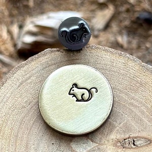 Peut inclure: Un gros plan d'un tampon en métal avec un motif de souris. Le tampon est sur une surface en bois.