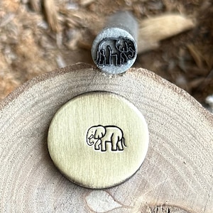 Op de afbeelding: Een close-up van een messing stempel met een olifantontwerp. De stempel bevindt zich op een houten oppervlak.