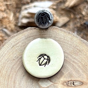 Puede incluir: Primer plano de un sello de latón con un diseño de escarabajo. El sello está sobre una superficie de madera.