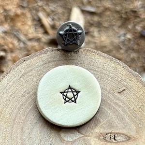 Puede incluir: Un primer plano de un sello de metal con un diseño de estrella de cinco puntas. El sello está sobre una superficie de madera y se ha utilizado para crear una impresión de la estrella en la superficie.