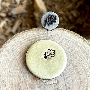 May include: Two metal stamps with an oak leaf design. The stamp on the left is brass and the stamp on the right is silver.