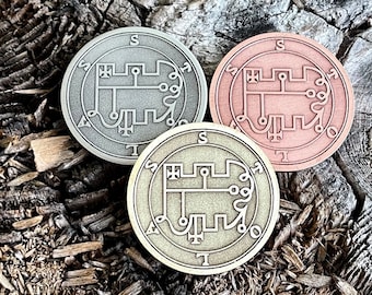 May include: Three round metal tokens with intricate designs. The tokens are silver, copper, and gold in color. Each token has a symbol in the center and a circle of text around the edge.