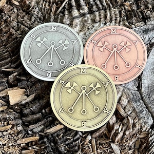 Könnte beinhalten: Drei Metallmünzen mit einem Symbol eines Pentagramms mit drei Spitzen auf einer Holzoberfläche. Die Münzen sind silber, kupfer und gold.