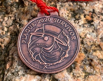 May include: A copper-colored pendant necklace with a red cord. The pendant features a plague doctor mask with the text "PLAGUE 2020 SURVIVOR".