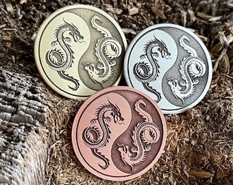 May include: Three yin yang metal pins with a dragon design. The pins are in gold, silver, and copper.
