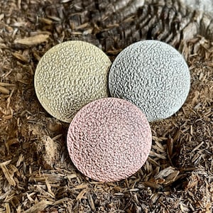 Könnte beinhalten: Drei runde Metallscheiben mit einer strukturierten Oberfläche. Die Scheiben sind gold, silber und roségold.