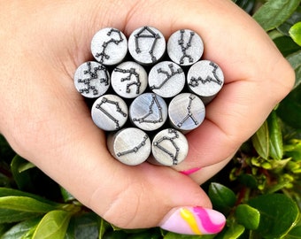 May include: A collection of eleven cylindrical metal stamping tools, each featuring a unique engraved constellation design on its flat circular face. The silver-toned steel rods are grouped together, displaying various star patterns.
