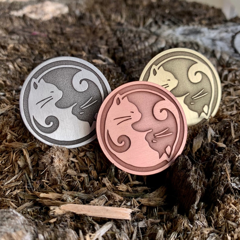 Op de afbeelding: Drie ronde metalen yin yang katten ontwerp pinnen. De pinnen zijn zilver, koper en goud. De katten kijken elkaar aan in een yin yang ontwerp.
