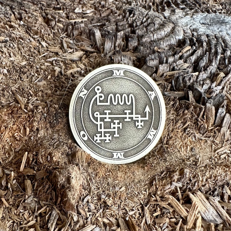 May include: A silver-colored metal coin with a sigil and the letters "M A O N I" around the edge.