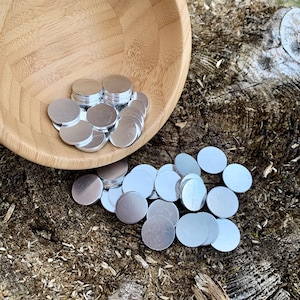 May include: A wooden bowl filled with silver metal discs, spilling out onto a rough, brown, wooden surface.