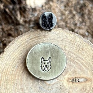 May include: Two metal stamps with German Shepherd dog designs. One stamp is a small, circular design with the dog's head. The other stamp is a larger, circular design with the dog's full face. The stamps are made of a metallic material.