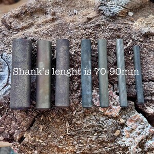 May include: A collection of cylindrical metal rods in varying shades of gray and brown, arranged on a textured wooden surface. The text "Shank's lenght is 70-90mm" is visible. The rods appear to be of different lengths and diameters.