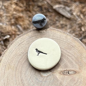 Puede incluir: Un primer plano de un sello de metal con la silueta de un pájaro. El sello está sobre una superficie de madera.