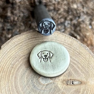 Puede incluir: Un sello de metal con un diseño de cara de perro sonriente. Junto a él, un círculo estampado con la misma cara de perro. El sello es de metal y se utiliza para crear impresiones en varios materiales.