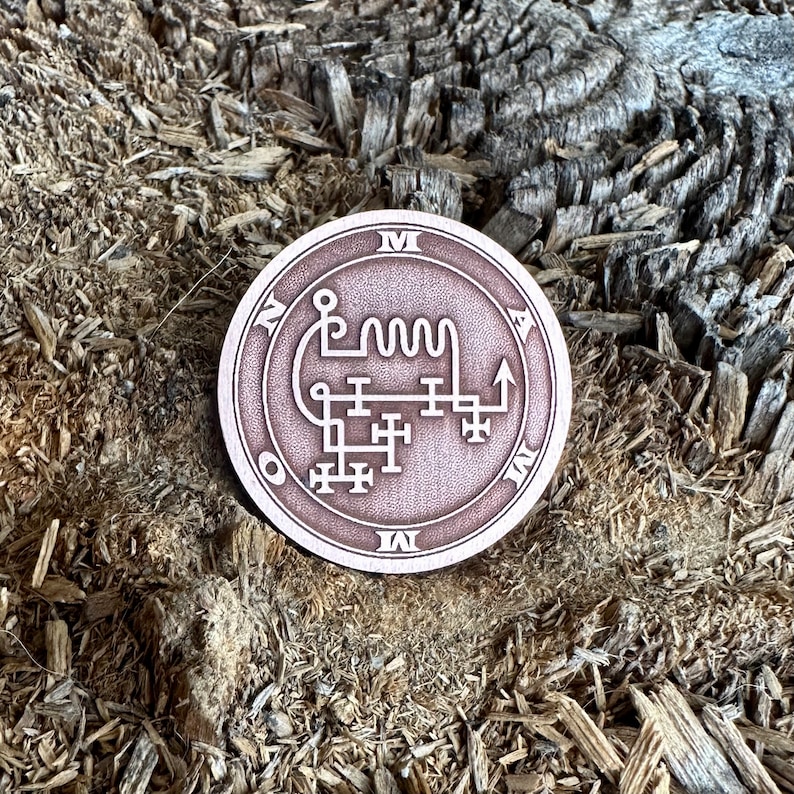 May include: A circular, copper-colored metal sigil with a white design. The sigil is inscribed with the letters "M", "A", "O", "I", and "N".