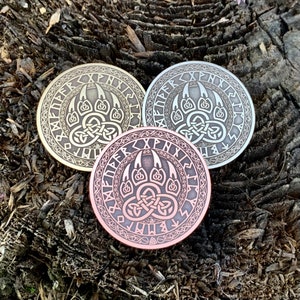 May include: Three round metal coins with a bear paw print design and runes around the edge. The coins are in gold, silver, and copper.