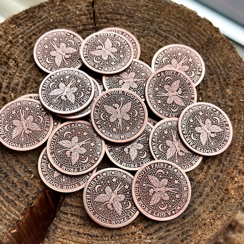 May include: A collection of round, copper-colored tokens with a fairy design. Each token features a fairy with wings, surrounded by stars and moons. The text "A Gift From Your Tooth Fairy" is inscribed on each token.