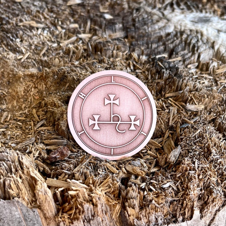 May include: A circular, copper-colored emblem featuring a central design of a cross with three additional crosses. The emblem has a border with the letters "H" and "L" visible. The emblem is set against a textured, wood-like background.