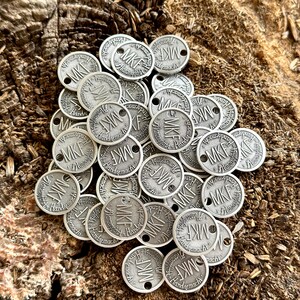 May include: A pile of silver-colored metal tokens with the letters "MKF" and the word "Handgemacht" engraved on them.